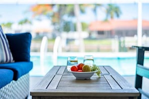 A poolside table with a bowl of fruit, a glass of water, and a glass of beverage. - Fish & Sips - Walking Distance to Cape Harbor - Kayak and Bikes - Intersecting Canal View (Cape Coral)