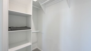 A white closet with shelves and a hanging rod, a door with a white handle, and a white ceiling. - 3 BEDROOM TOWNHOUSE - 28 (Yamba, Clarence Valley)