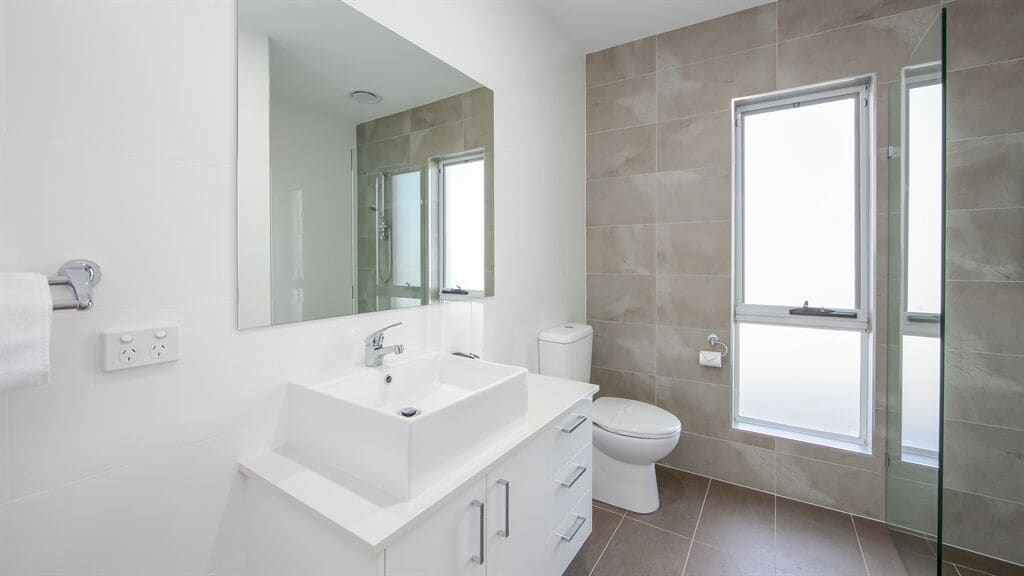 A modern bathroom with a large mirror, white sink, and toilet.
