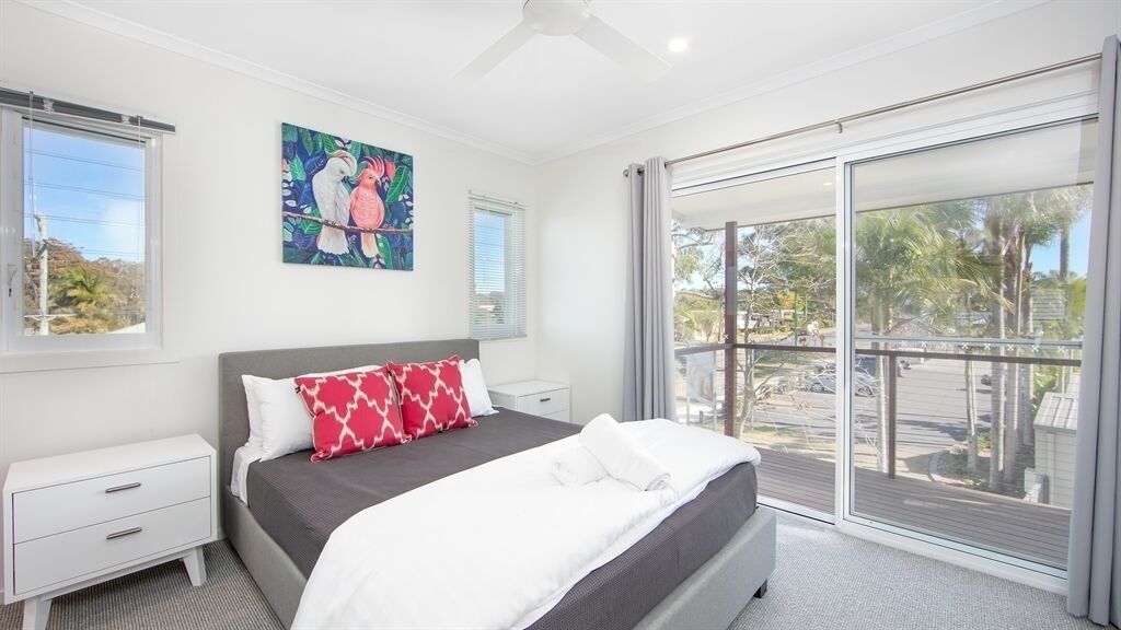 A bedroom with a bed, a nightstand, a window, and a painting on the wall.