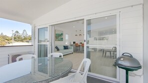A balcony with a glass table and chairs, a grill, and a view of the interior dining area. - 3 BEDROOM TOWNHOUSE - 28 (Yamba, Clarence Valley)
