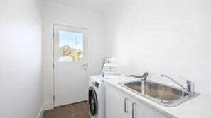 A compact laundry area with a washing machine, a drying rack, and a sink. - 3 BEDROOM TOWNHOUSE - 28 (Yamba, Clarence Valley)