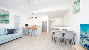 A modern living room with a sofa, dining area with chairs, a kitchen with a refrigerator, and artwork on the walls. - 3 BEDROOM TOWNHOUSE - 28 (Yamba, Clarence Valley)