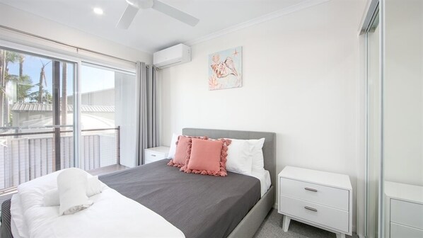 A modern bedroom with a bed, nightstands, a window with a view, and a ceiling fan. - 3 BEDROOM TOWNHOUSE - 28 (Yamba, Clarence Valley)