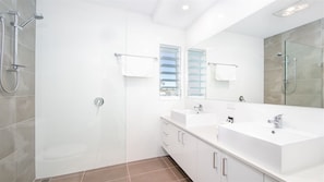 Un baño moderno con un espejo grande, dos lavamanos, una zona de ducha y un ventanal.