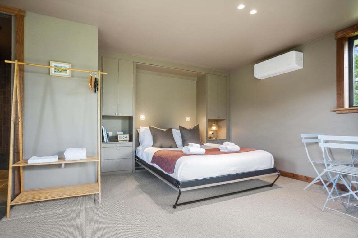 A bedroom with a bed, bedside tables, a wardrobe, a mirror, a window, and an air conditioning unit.