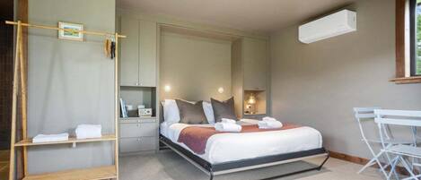 A bedroom with a bed, bedside tables, a wardrobe, a mirror, a window, and an air conditioning unit.