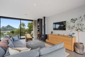 Ein modernes Wohnzimmer mit einer großen Couch, einem Holzschrank, einem Fernseher und Blick ins Freie.