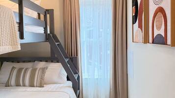 A bedroom with a bunk bed, a desk, a chair, a window with curtains, and abstract wall art.