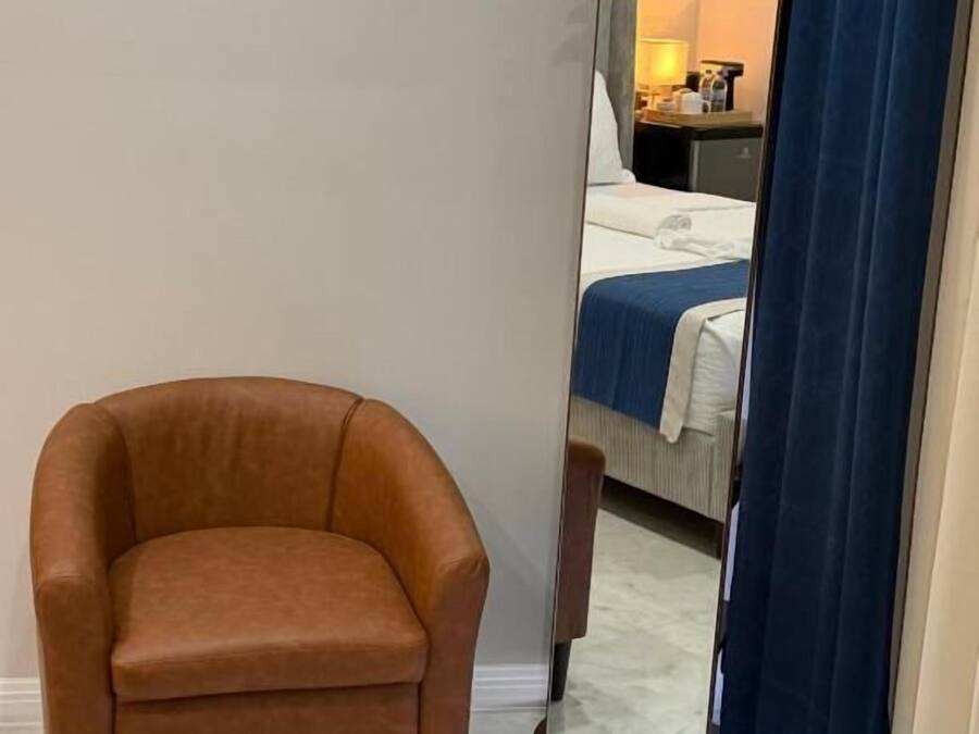A hotel room with a bed, a chair, a mirror, and a thermostat on the wall.