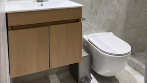 A bathroom with a white sink, wooden cabinets, a round mirror, a toilet, and a shower area. - Sanrai (Gros Islet)