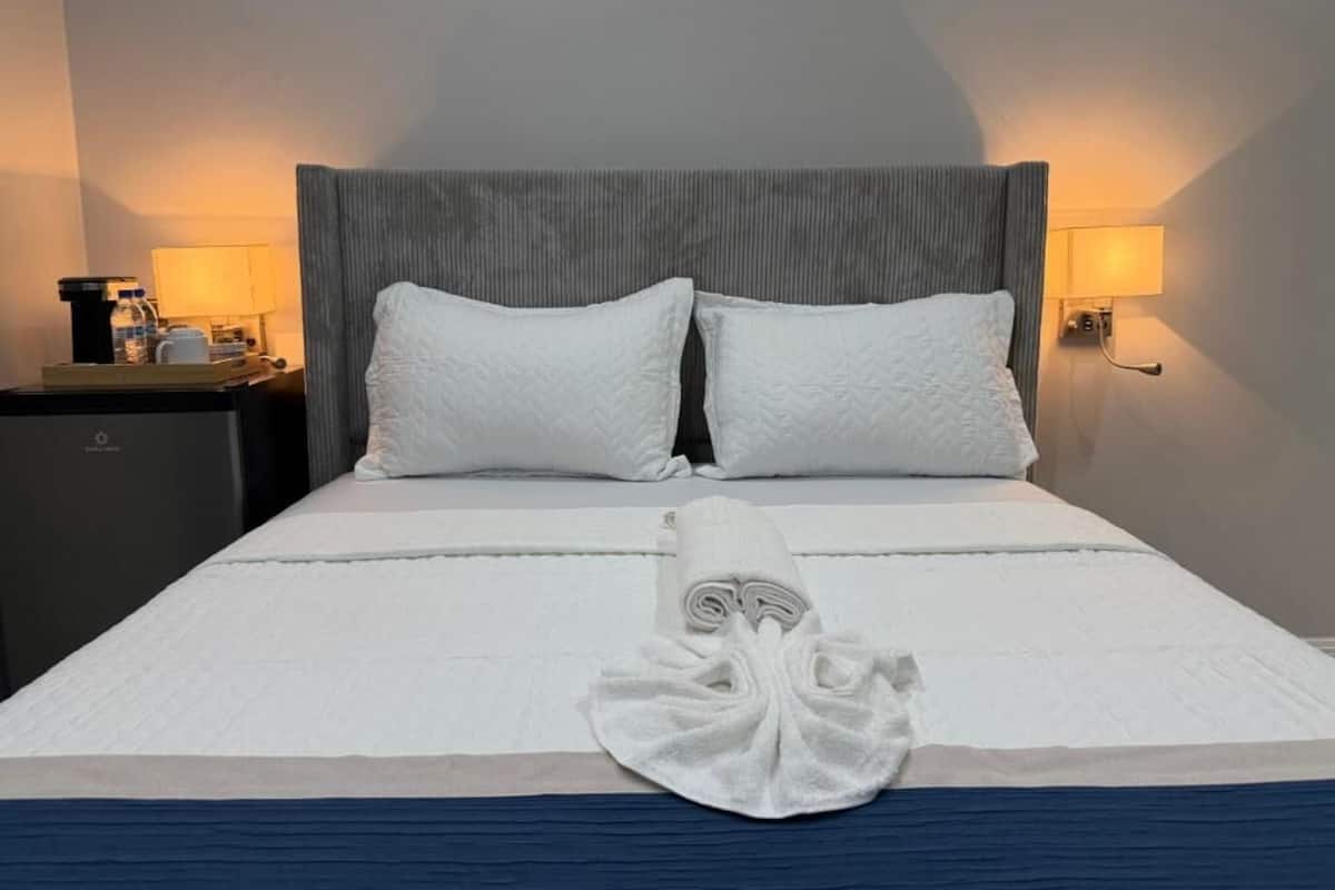 A neatly made bed with a folded towel, two pillows, and a headboard with a light fixture on either side.