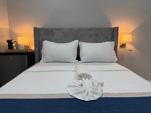 A neatly made bed with a folded towel, two pillows, and a headboard with a light fixture on either side. - Sanrai (Gros Islet)
