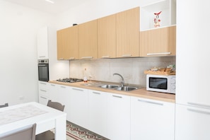 A modern kitchen with white cabinets, a gas stove, a microwave, and a sink. - Dimora Mennule Mare - Salento Reservation (Alliste)