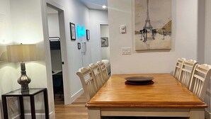 A dining room with a wooden table, white chairs, a painting of the Eiffel Tower, and a lamp on a side table. - A Vibrant Downtown Retreat for Groups, The Gallery (Halifax)