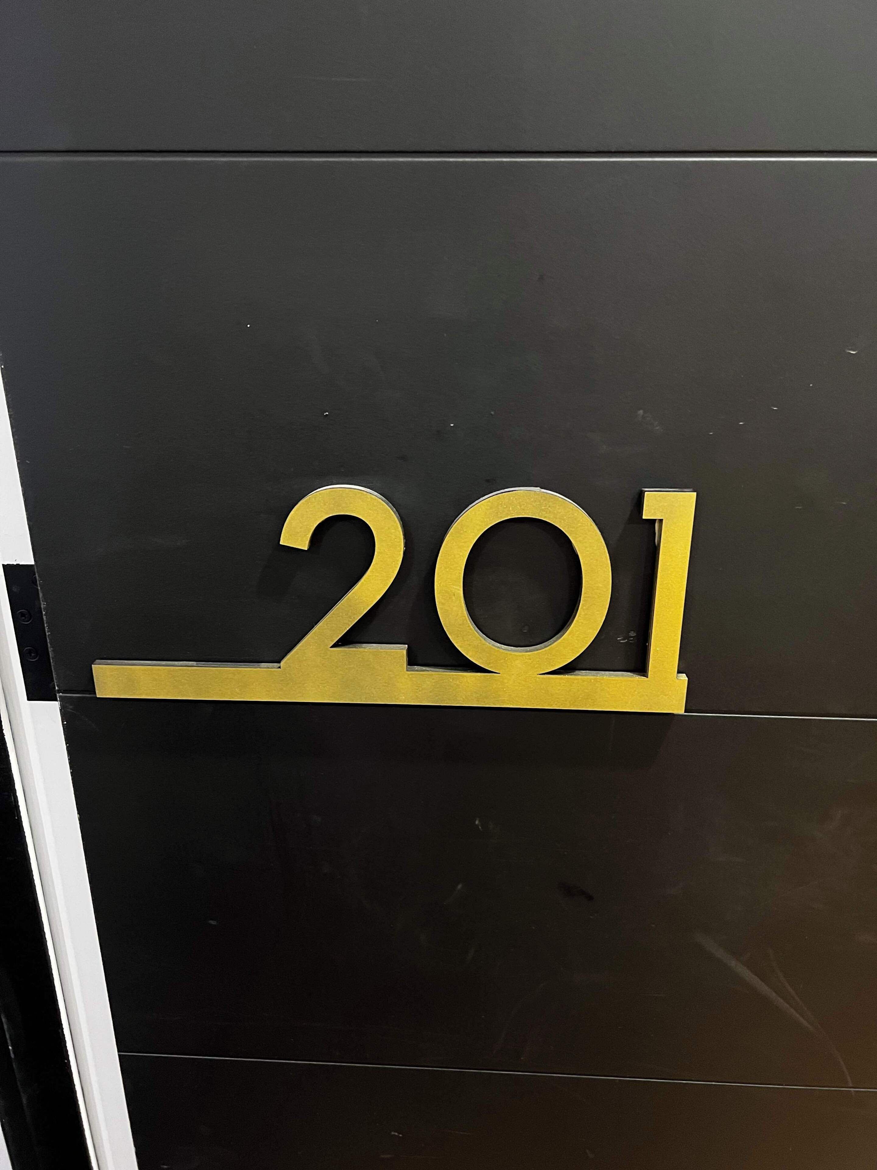 A black wall with a gold number '201' indicating a room or section number.