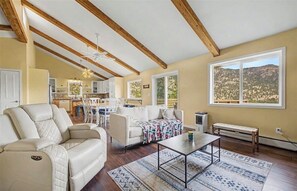Ein geräumiges Wohnzimmer mit einer Couch, einem Couchtisch und Blick auf eine Berglandschaft durch ein großes Fenster.