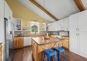Eine Küche mit Holzschränken, einer Mittelinsel, blauen Hocker und Pendelleuchten.