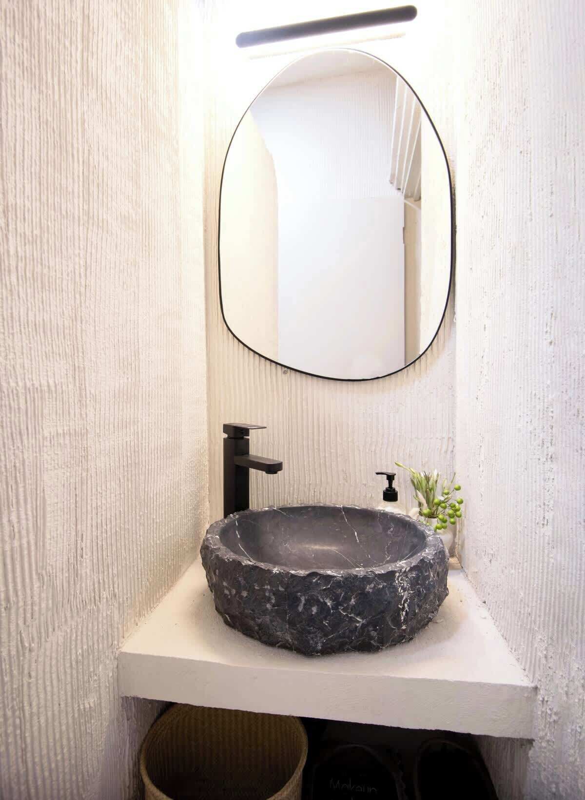 Un baño con un lavabo de piedra redondo, un grifo negro, un espejo rectangular y una planta pequeña en la encimera.