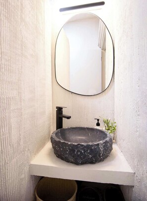 Un baño con un lavabo de piedra redondo, un grifo negro, un espejo rectangular y una planta pequeña en la encimera.