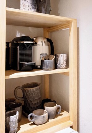 Una estantería con distintos utensilios de cocina, como una cafetera, tazas y un hervidor.