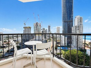 Uma varanda com vista para a cidade, cadeiras brancas, uma mesa pequena e um corrimão.