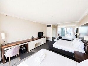 Ein Hotelzimmer mit Bett, Schreibtisch, Stuhl, Fernseher und Fenster mit Blick auf die Stadt.