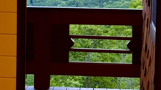 Blick durch ein Fenster mit Holzrahmen auf eine gebirgige Landschaft mit dichten grünen Wäldern und ferne Hügel.