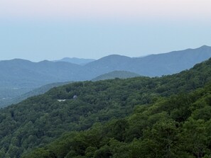A mountainous landscape with dense forest and a small building on a hill.