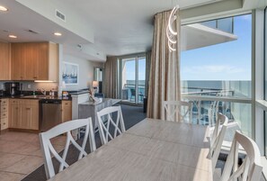 A modern kitchen with a dining area, a view of the sea, and a balcony with a glass railing. - Large 2BR at Oceans One Resort  with Best Ocean View (Myrtle Beach)
