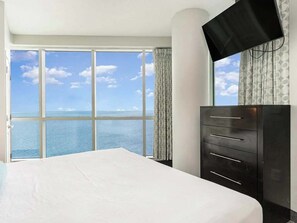 Ein Hotelzimmer mit großem Fenster, einem Bett, einem Schminktisch und einem Fernseher.