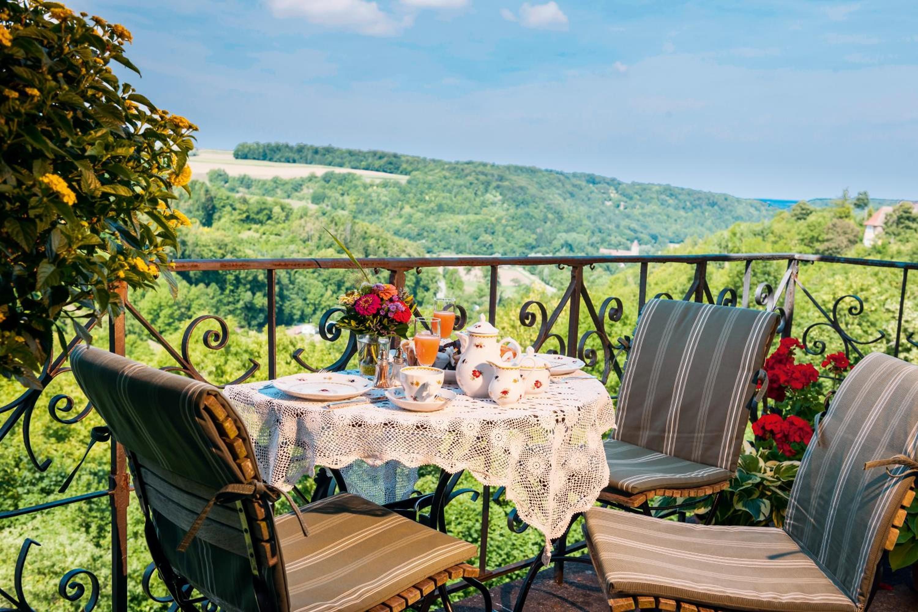 An outdoor dining area with a table set for two, surrounded by chairs, and overlooking a scenic landscape.