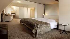 Una camera d'albergo con un letto grande, un'area salotto con un divano e un tavolino con una lampada.