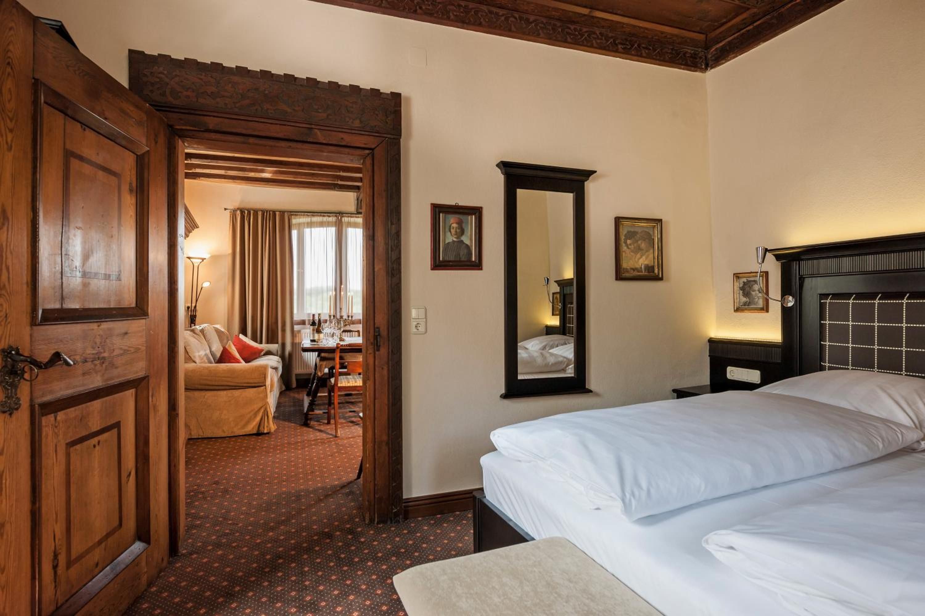Une chambre d’hôtel avec un grand lit, un coin salon comprenant un canapé et une table, un miroir et une porte donnant sur une autre pièce.