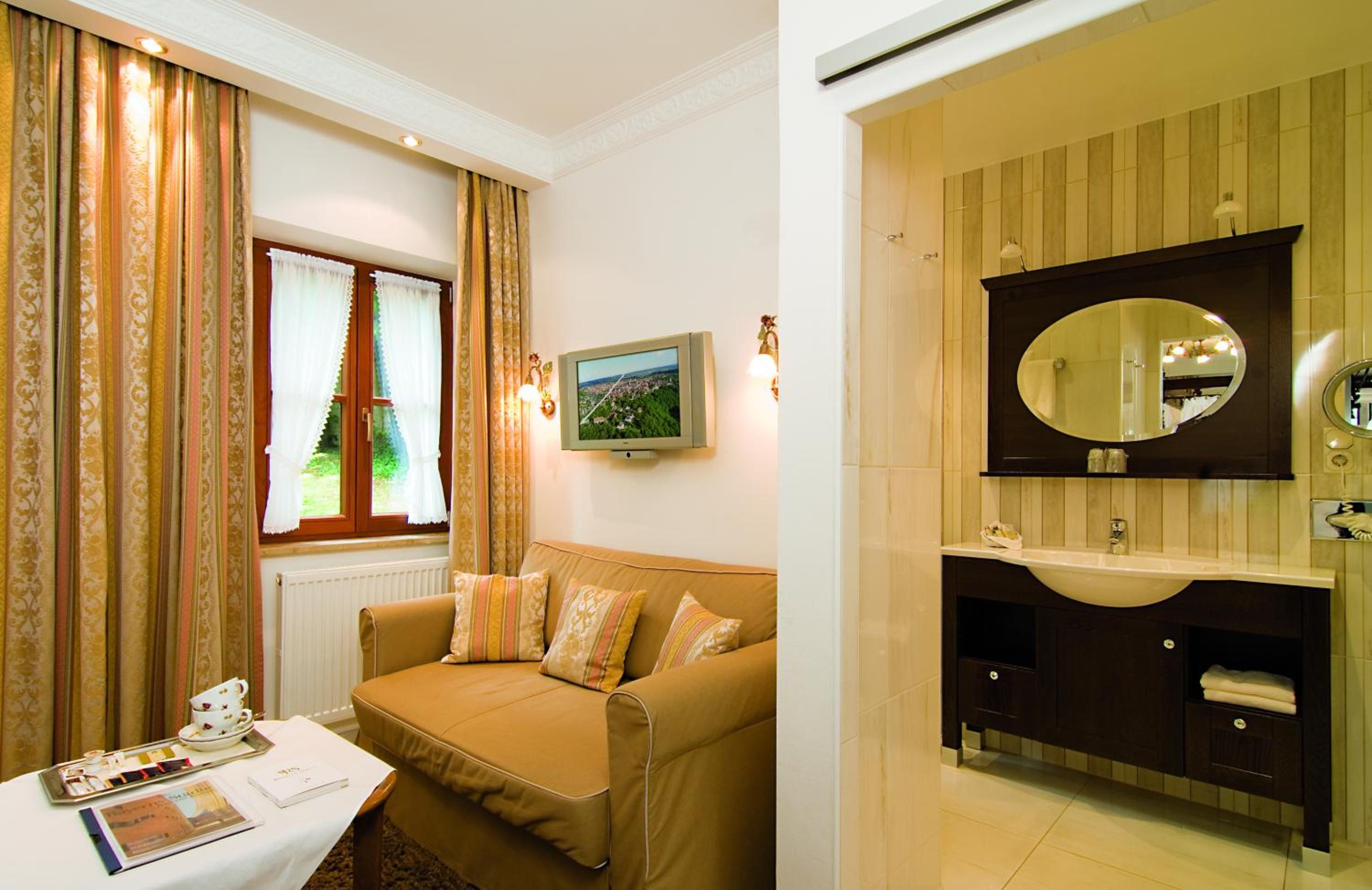 Habitación de hotel con sofá, una mesa con bandeja de té, televisión y baño con espejo y lavamanos.