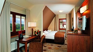 Una camera d'albergo con un letto, una scrivania, una sedia, una televisione e una finestra con tende.