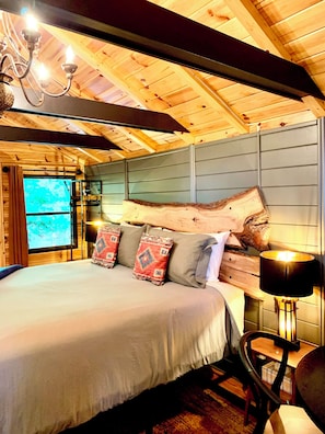 Um interior de madeira com uma cama, almofadas, um candelabro e uma janela.