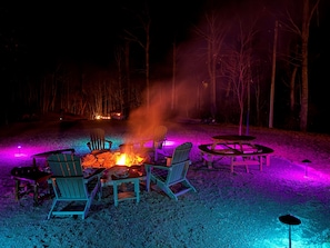 Ein Außenbereich mit Sitzgelegenheiten bei Nacht, inklusive Feuerstelle, Stühlen und Tischen.