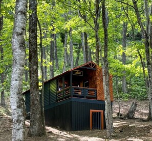 Une cabane en bois, située dans une forêt, dotée d’un balcon et d’une enseigne indiquant le mot « Lodge ».