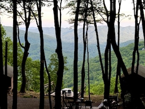 Ein bewaldetes Gebiet mit Blick auf ferne Hügel, eine Holzterrasse und ein kleiner Tisch mit Stühlen.