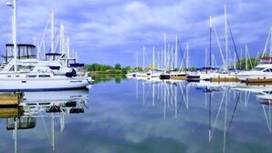 Una marina con varios veleros amarrados, agua tranquila y cielo despejado.