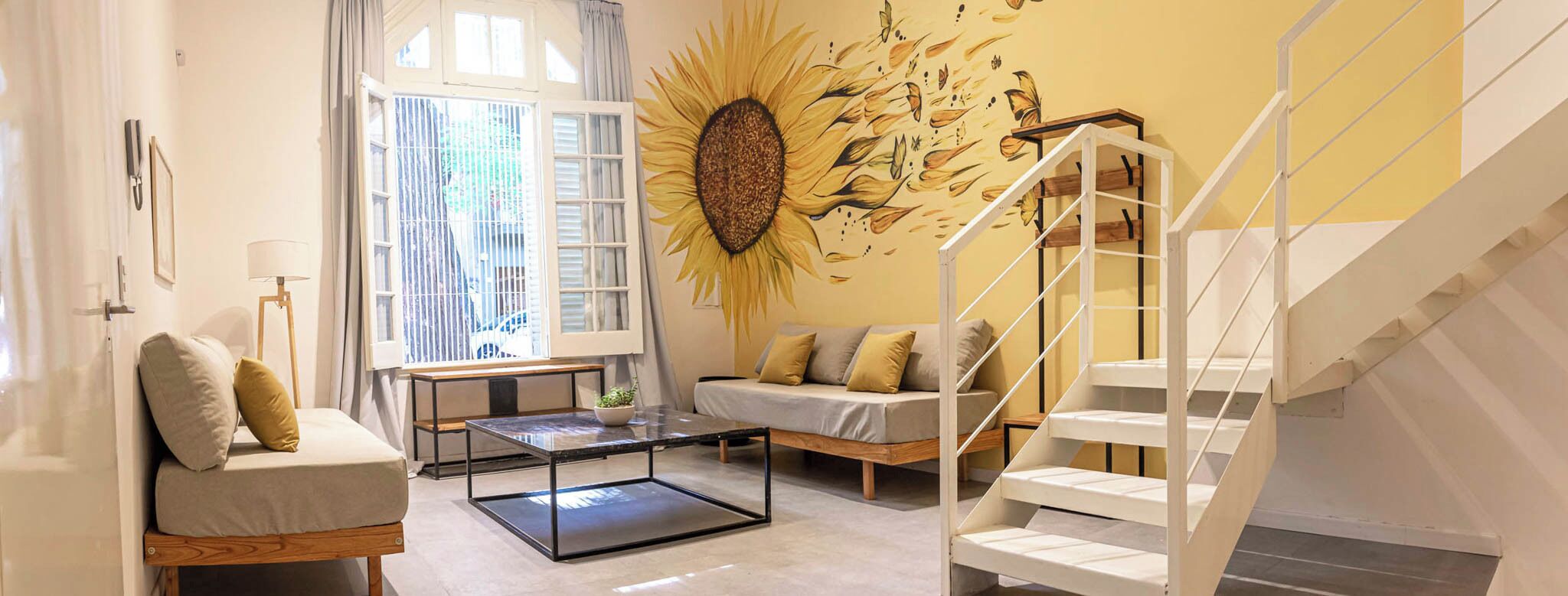 Ein modernes Wohnzimmer mit einer Couch, einem Couchtisch, einer Treppe und einem Wandgemälde mit einem Sonnenblume.
