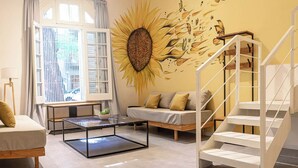 En moderne stue med sofa, sofabord, trappe og et solblomstermotiv på væggen.