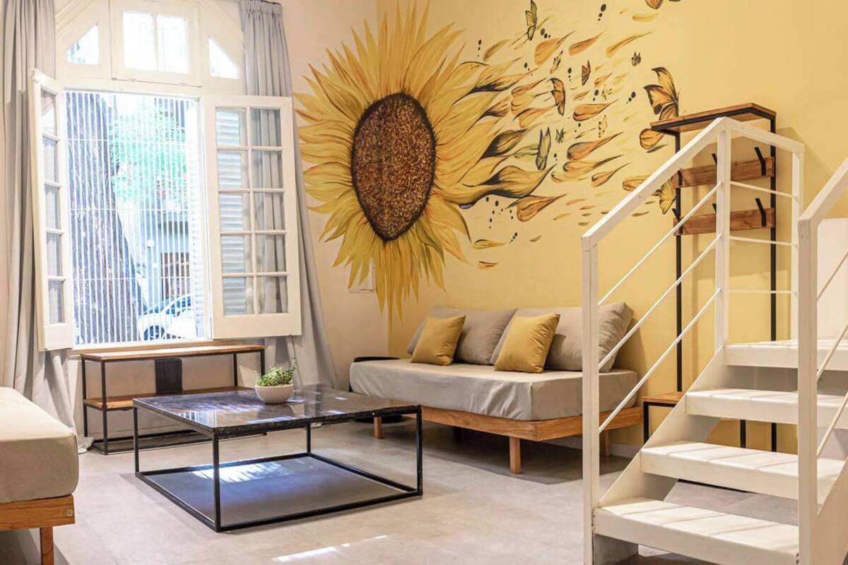 A modern living room with a sofa, a coffee table, a staircase, and a mural of a sunflower.
