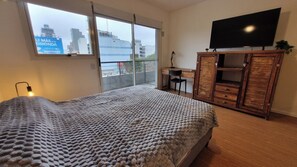 Ein Schlafzimmer mit einem Bett, einem Schreibtisch, einem Fernseher und Blick auf die Stadt durch ein Fenster.