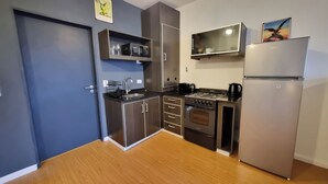 Een kleine keuken met een magnetron, fornuis en koelkast, houten vloeren en donkerblauwe muren.