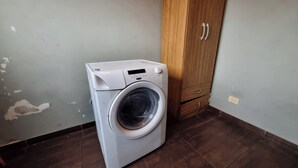 Een compacte, witte wasmachine in een kamer met een houten garderobe en een betegelde vloer.