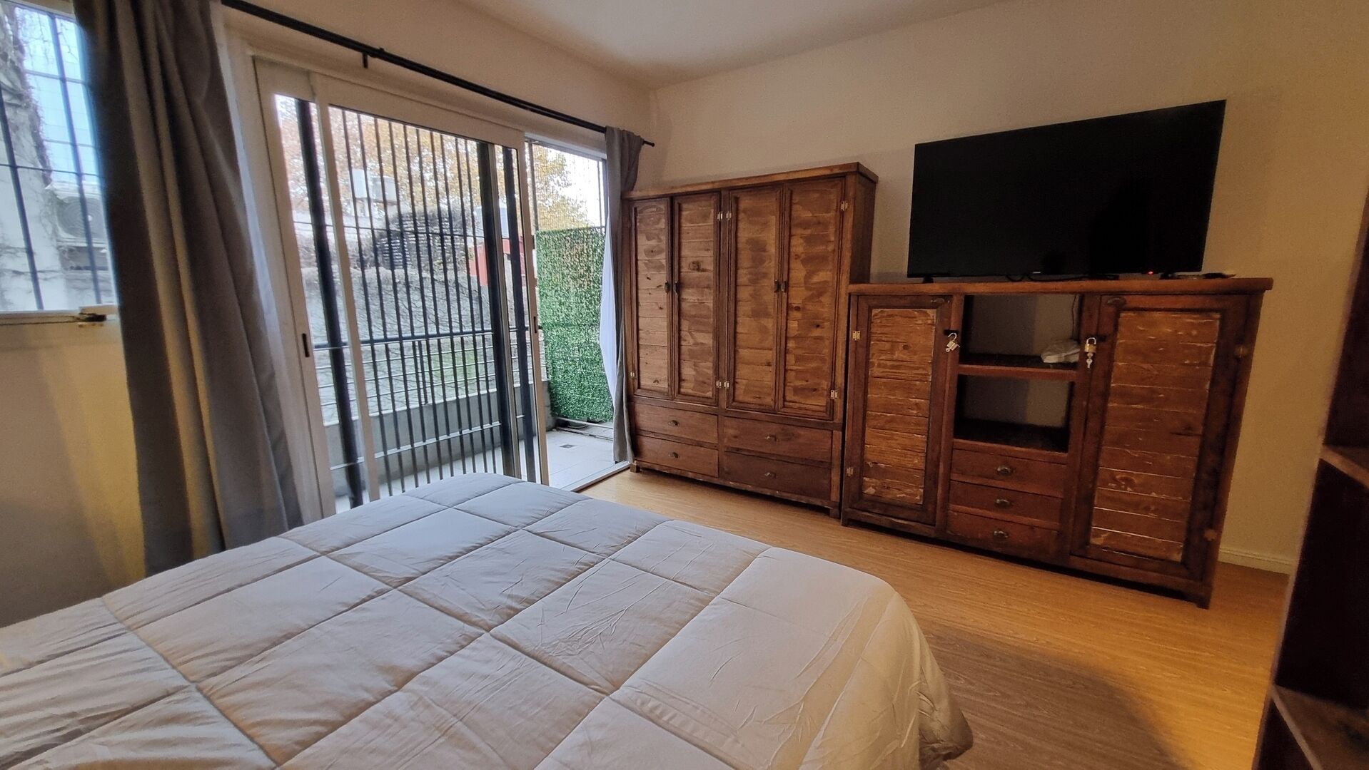 Une chambre à coucher comprenant un lit, une armoire, un téléviseur et une porte-fenêtre coulissante donnant sur un balcon.