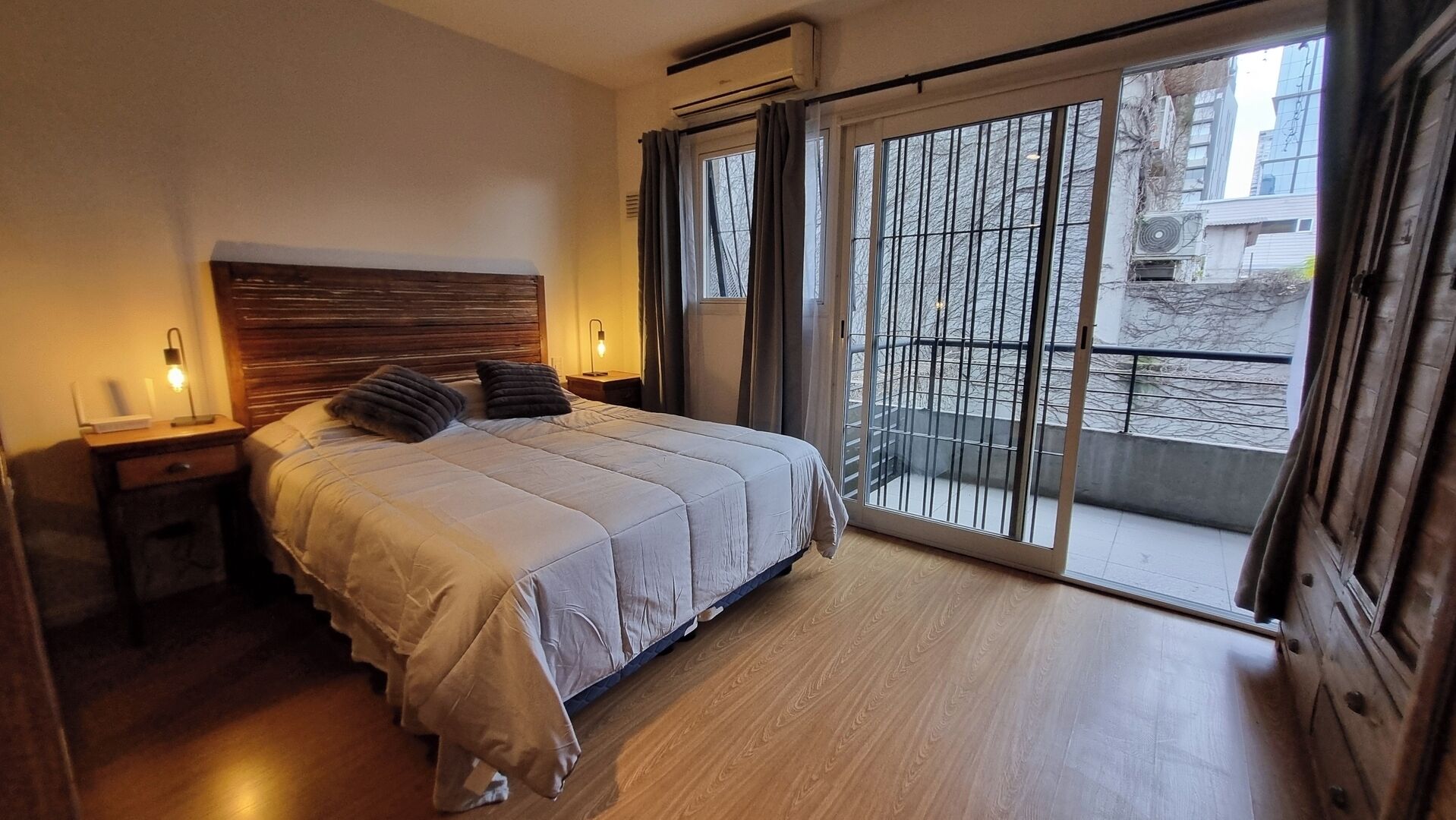 A bedroom with a bed, bedside tables, a window with curtains, and a view of the outside.