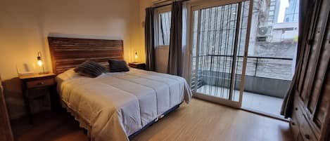 A bedroom with a bed, bedside tables, a window with curtains, and a view of the outside.